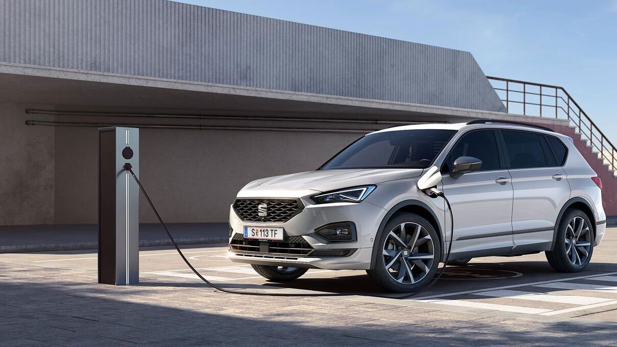 Silberner Seat Tarraco Elektroauto an einer Ladestation in einer modernen Umgebung.