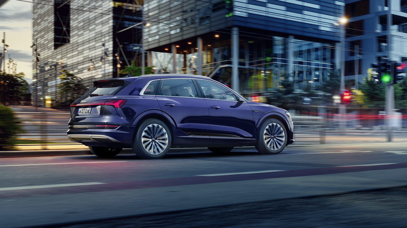 Audi Q8 in Bewegung auf einer urbanen Straße mit Wolkenkratzern im Hintergrund.