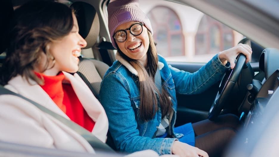 Zwei Freundinnen lachen und genießen die Fahrt im Auto.